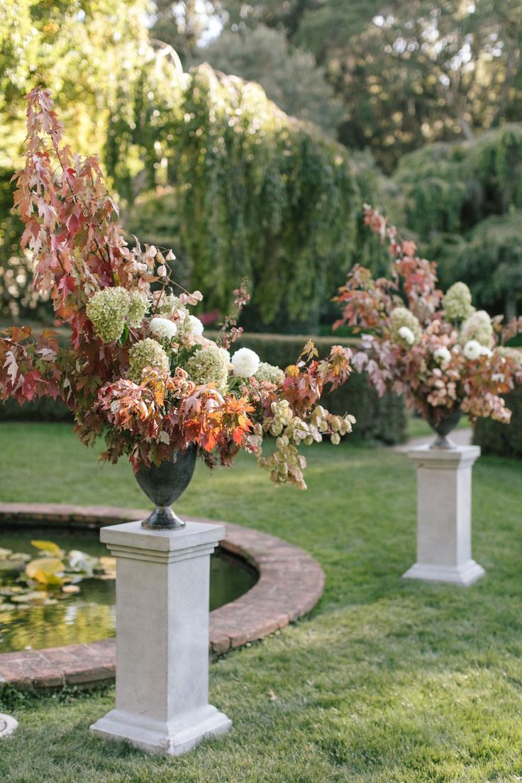 three vases filled with flowers sitting on top of a lush green field next to a pond