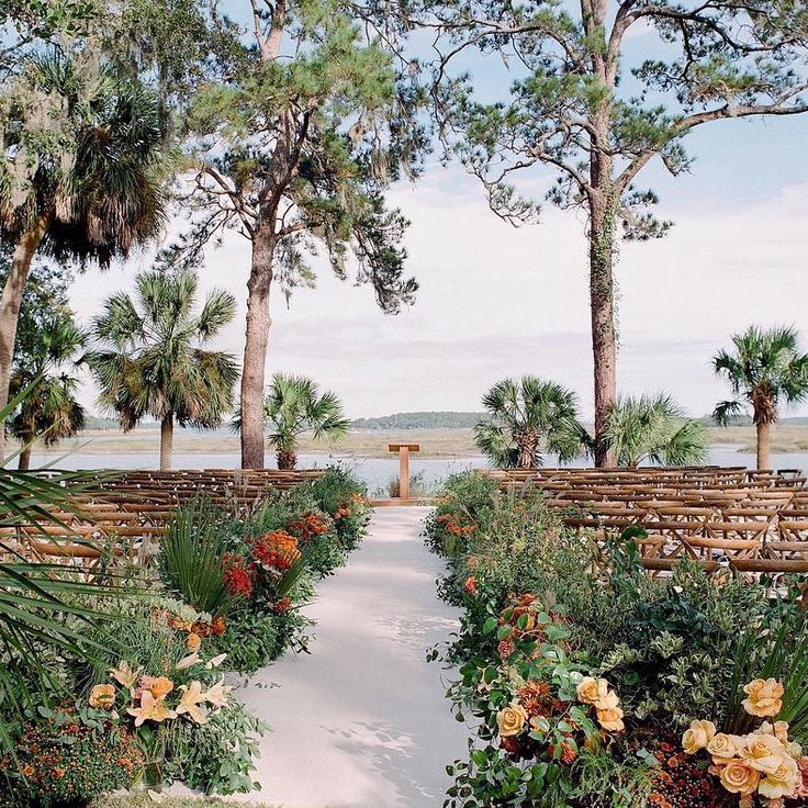 an outdoor ceremony setup with chairs and flowers in the foreground, surrounded by palm trees