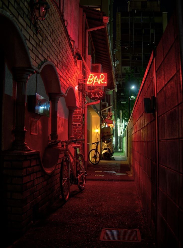 a bike is parked on the side of a building with a neon bar sign above it