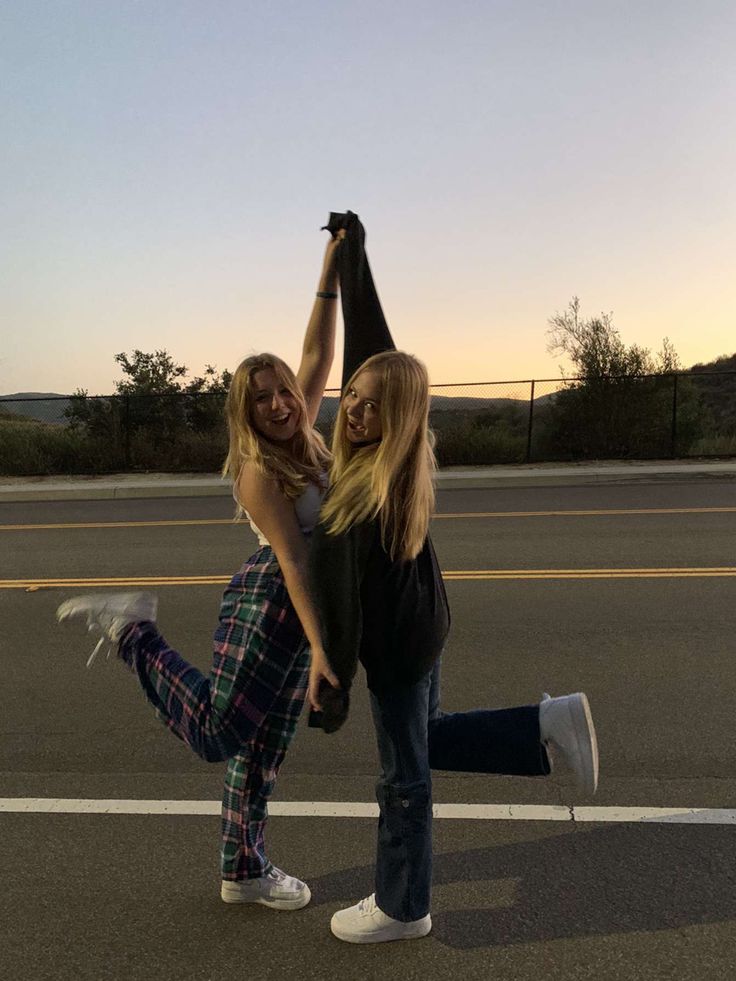 two women standing in the middle of an empty parking lot, one holding up her leg