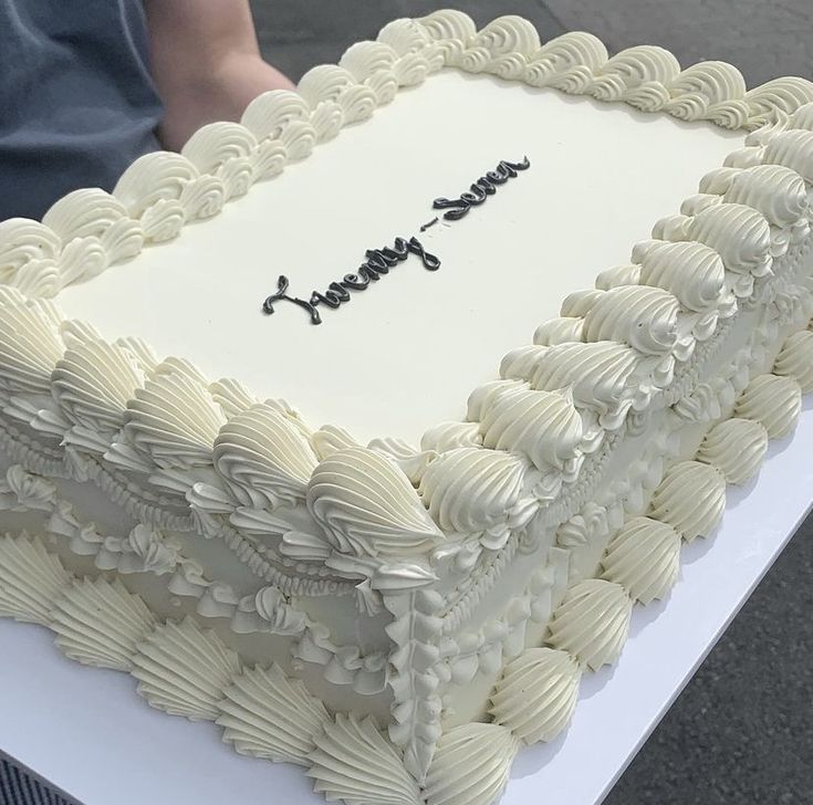 a large white sheet cake sitting on top of a table next to a persons hand