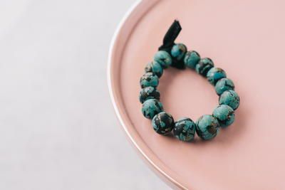 a bracelet made out of turquoise beads on a pink plate with a black ribbon around it