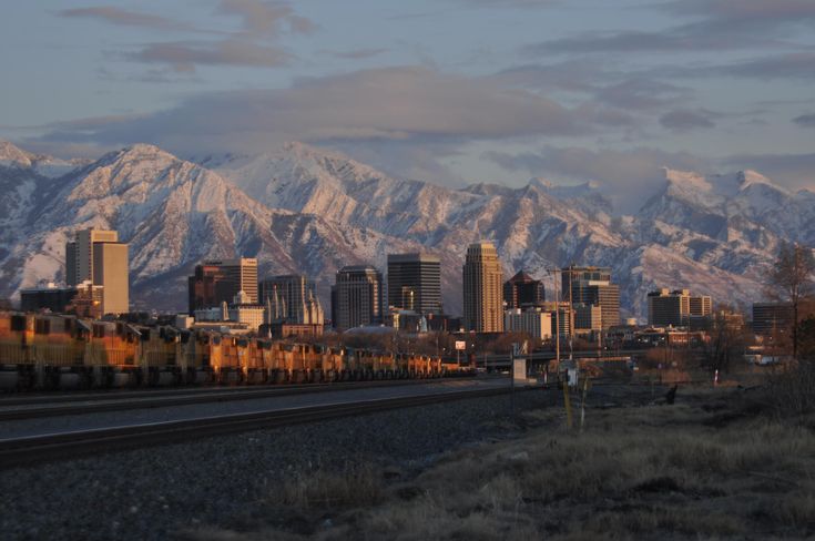 a train traveling through a city with snow covered mountains in the backgroung