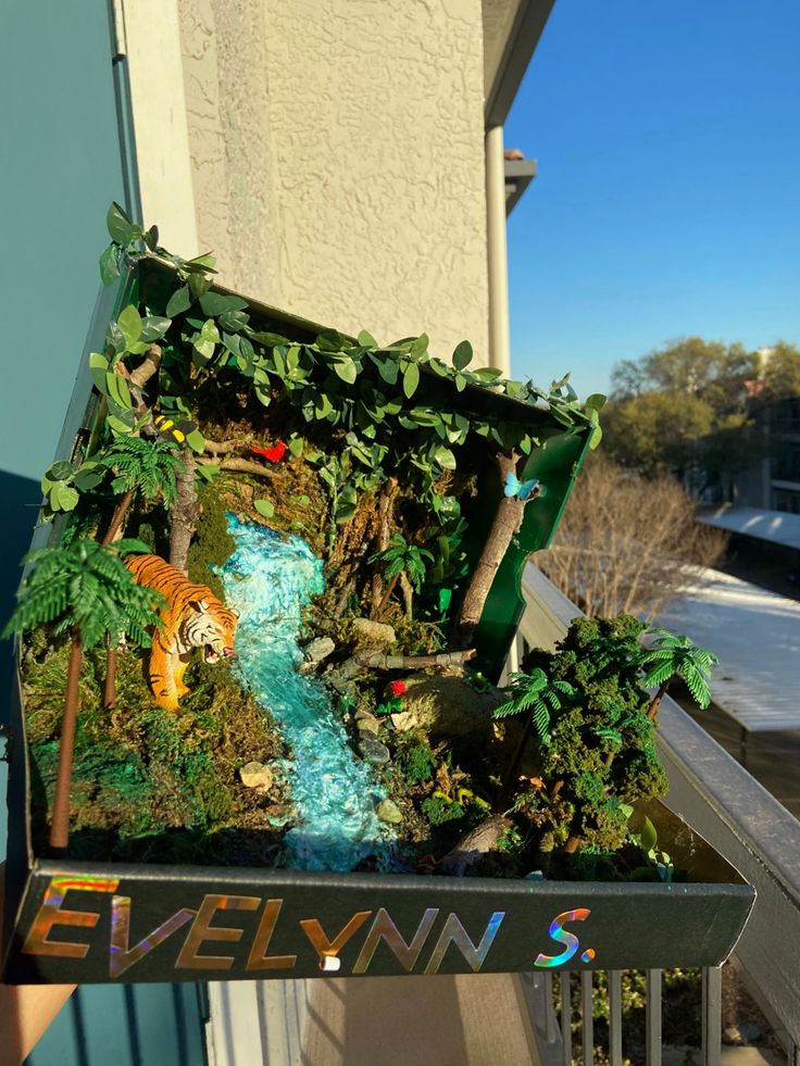 a box filled with fake plants and animals on top of a balcony next to a building