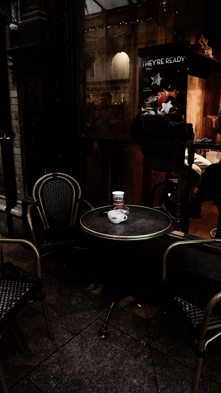 two chairs and a table with a cup on it in a dark room next to a piano