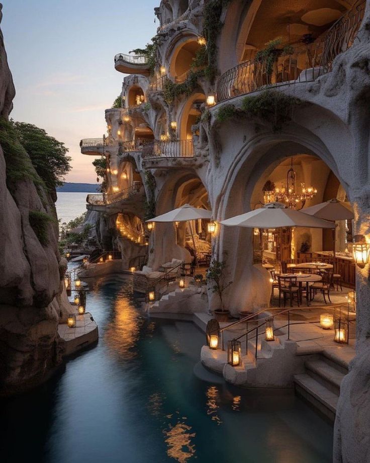 an outdoor restaurant with candles lit up next to the water and cliffs in the background