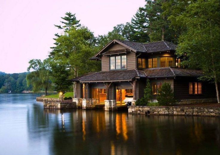 a large house sitting on top of a lake next to a lush green forest covered hillside