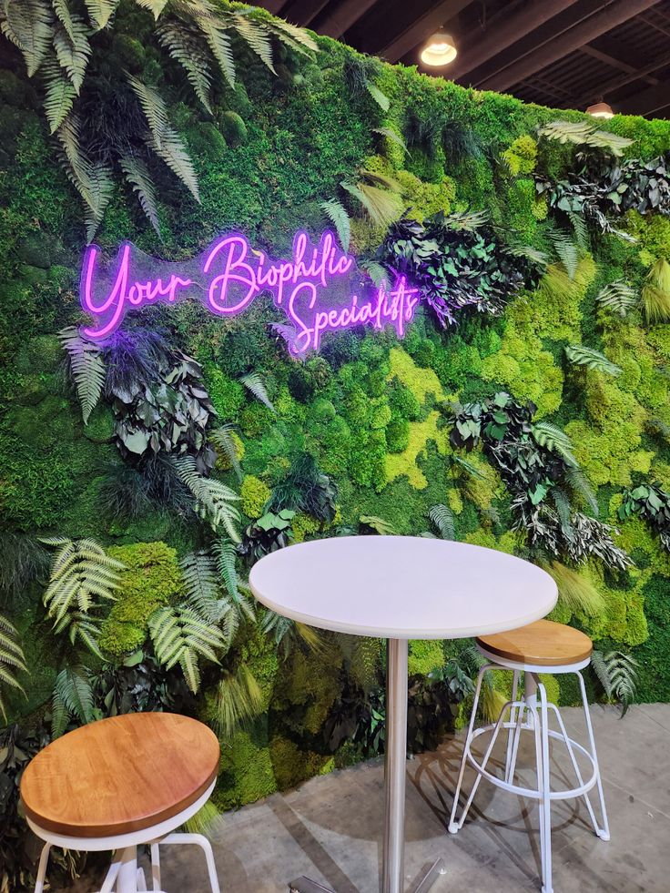 two stools sit in front of a green wall with plants and words on it