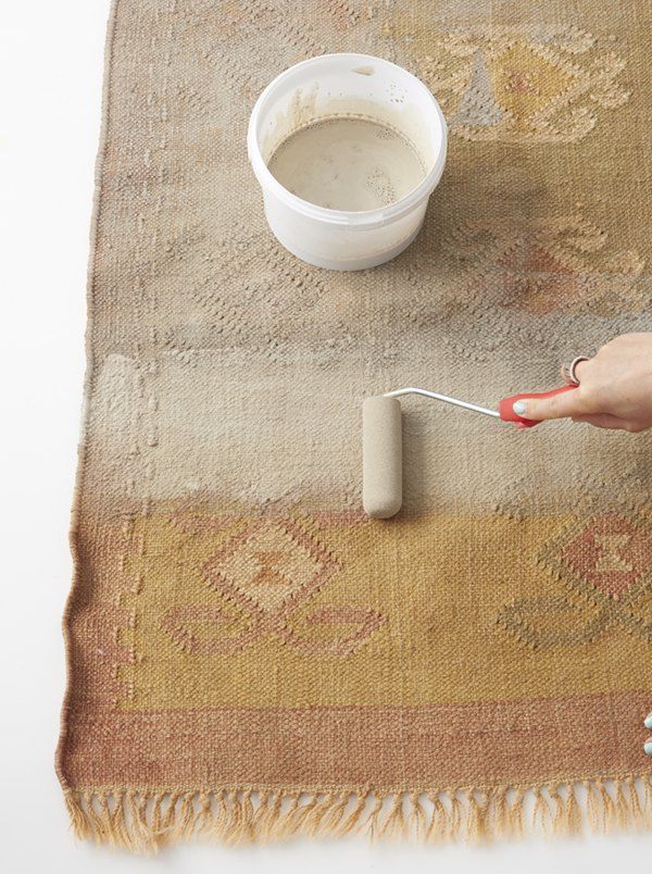 a person is using a paint roller on a rug with a cup of white liquid