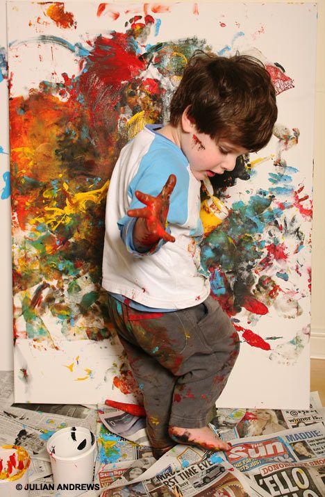 a young boy standing on top of a pile of newspaper next to an art work