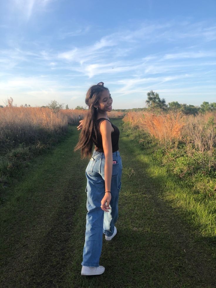 a girl standing in the middle of a dirt road with her hand on her hip