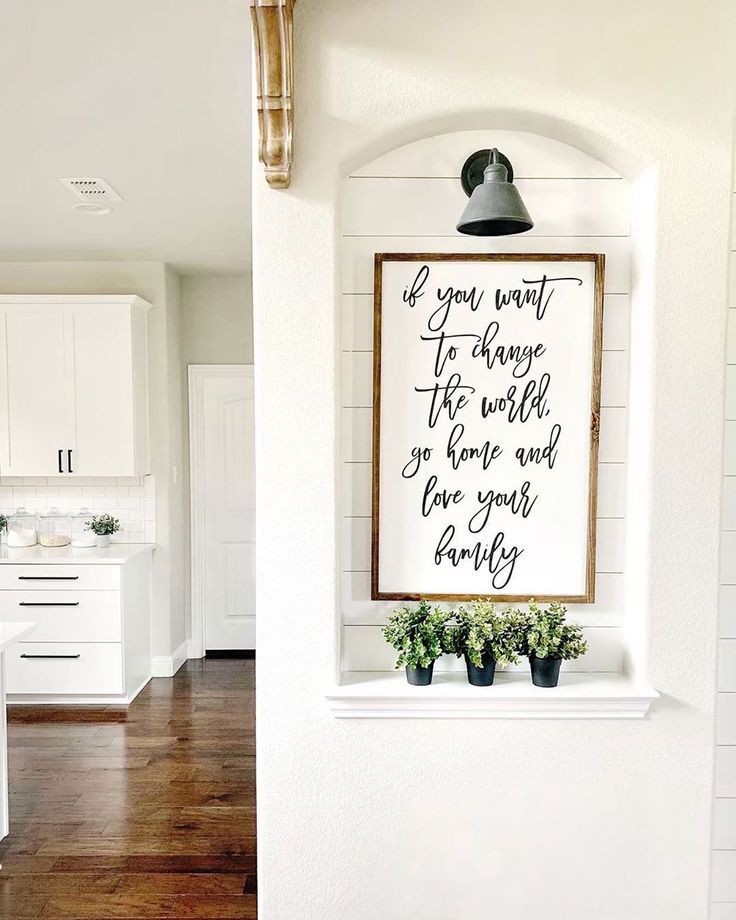 a kitchen with white cabinets and wood flooring next to a framed sign that says if you want to change the world, go home and love your country