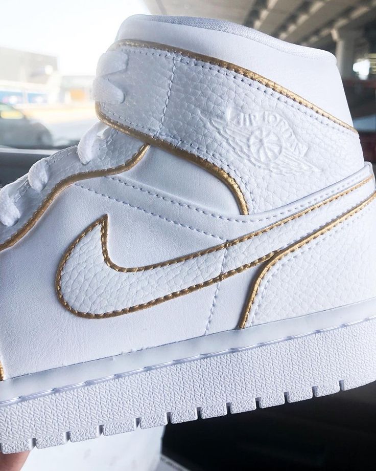 someone holding up a white and gold nike shoe