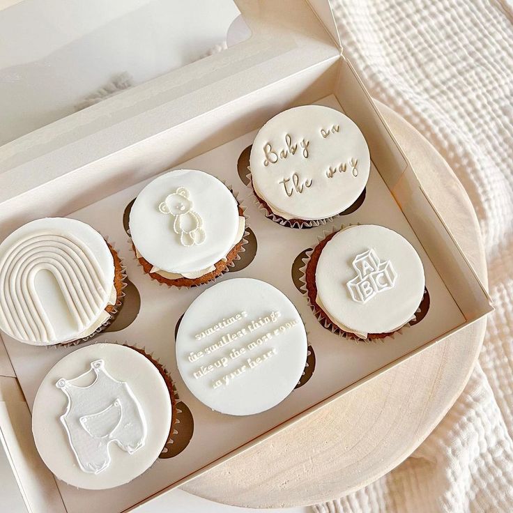 four cupcakes with white frosting in a box on a table next to a blanket