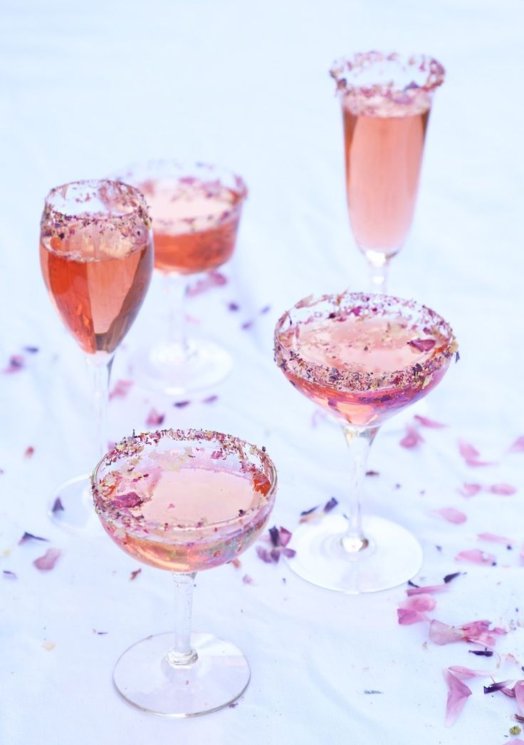 three glasses filled with pink liquid on top of a white table covered in rose petals