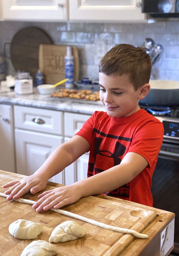 a little boy that is standing in front of a cutting board with doughnuts on it