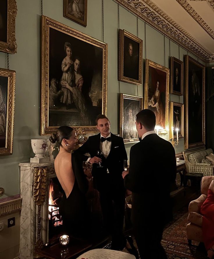 a man and woman in formal wear standing next to each other with paintings on the wall behind them