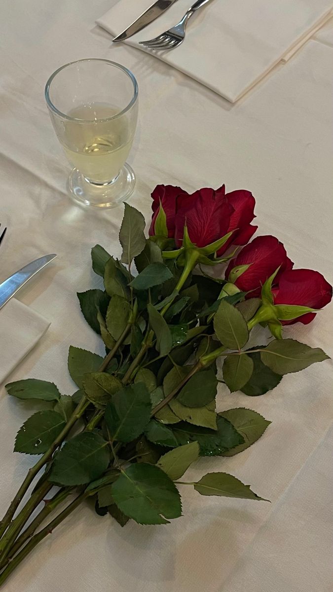 a bouquet of roses sitting on top of a white table cloth next to a knife and fork