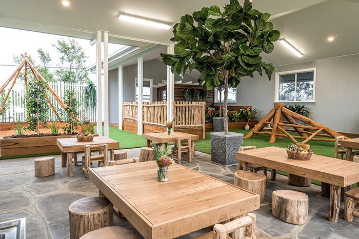 an outdoor restaurant with wooden tables and benches, potted plants and artificial grass in the background