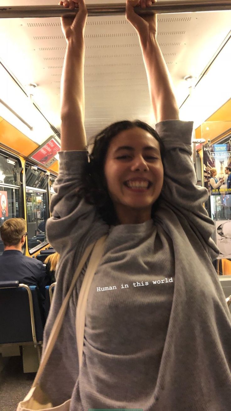 a woman holding her arms up in the air on a bus with people sitting down