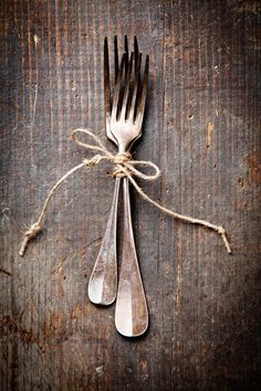 two forks tied up to each other on top of a wooden table next to a string