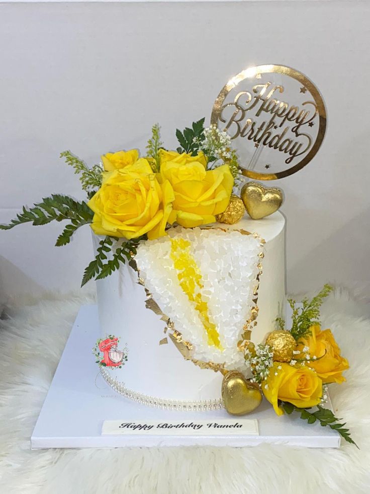 a birthday cake decorated with yellow roses and greenery sits on a white furnishing