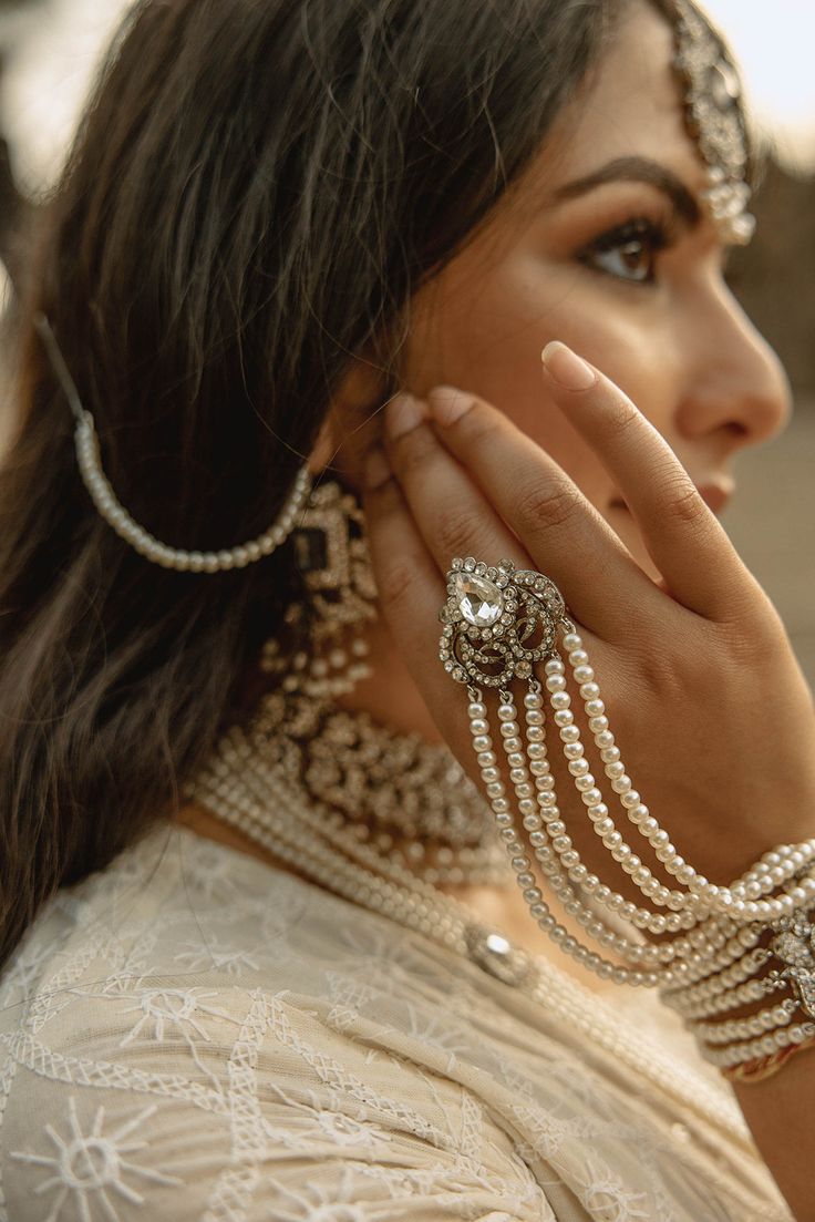 The Sanzida Silver & Pearl Full Bridal Set is an exquisite, handcrafted collection designed for the perfect South Asian wedding. This bridal set includes a choker necklace set, long haar, maang tikka, jhoomer, and two haathphool with attached rings. Made from silver plating, this stunning bridal jewelry features zircon stones in white and a clear grayish center stone, complemented by cascading faux pearls. Ideal for Pakistani jewelry enthusiasts, this bridal set is a must-have for any bride. Key Pearl Bridal Jewelry Indian, Festive Chandbali Bridal Sets With Intricate Design, Elegant Silver Anarkali Set For Wedding, Elegant Bridal Accessories With Intricate Design For Festive Occasions, Bollywood Style Cutdana Tikka For Wedding, Elegant Festive Bridal Accessories With Intricate Design, Silver Kundan Bridal Sets With Cutdana, Kundan Bridal Sets In Silver With Cutdana, Elegant Kundan Bridal Sets For Eid