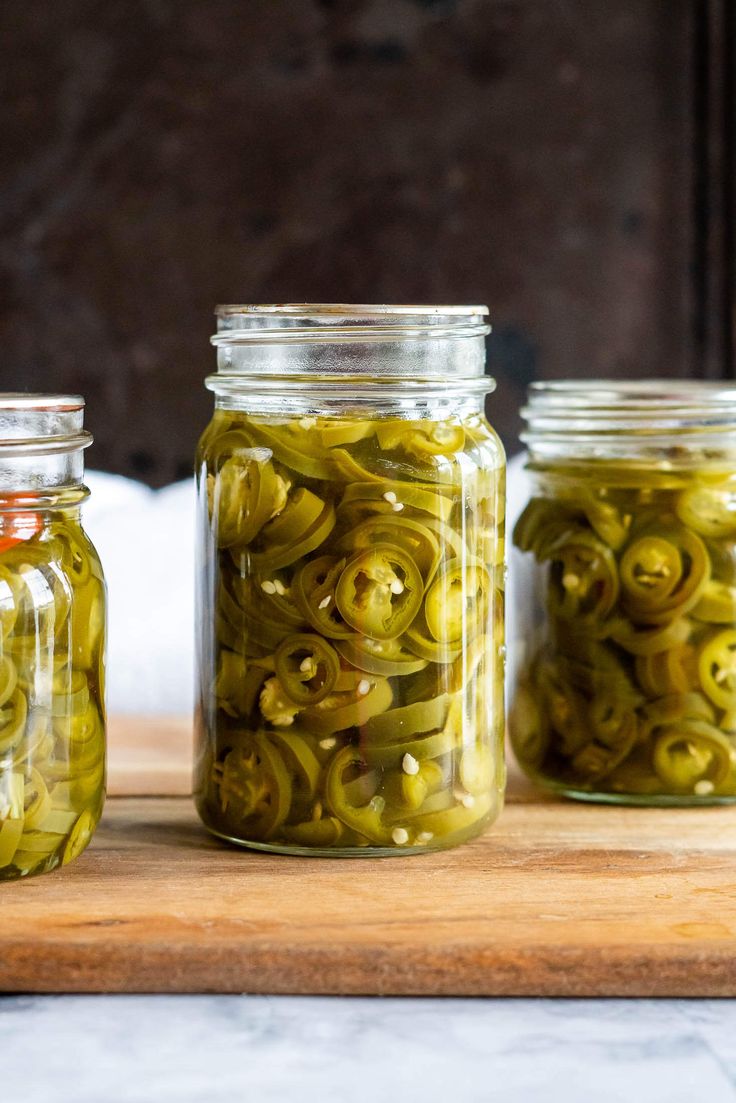 three jars filled with pickles sitting on top of a wooden table