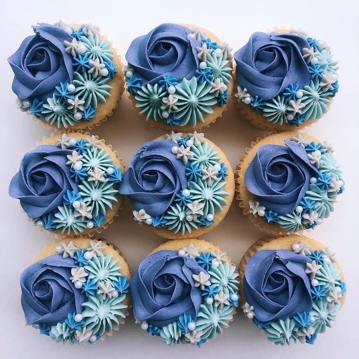 twelve cupcakes with blue frosting and white flowers on them are arranged in a square pattern