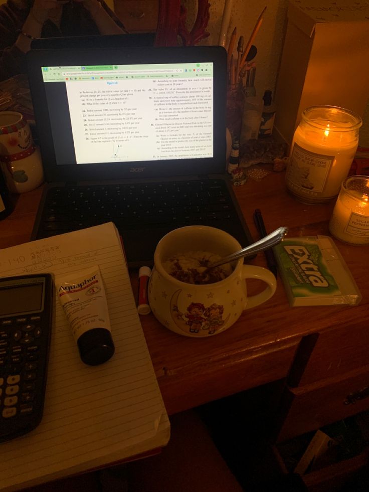 a laptop computer sitting on top of a wooden desk next to a cup of cereal