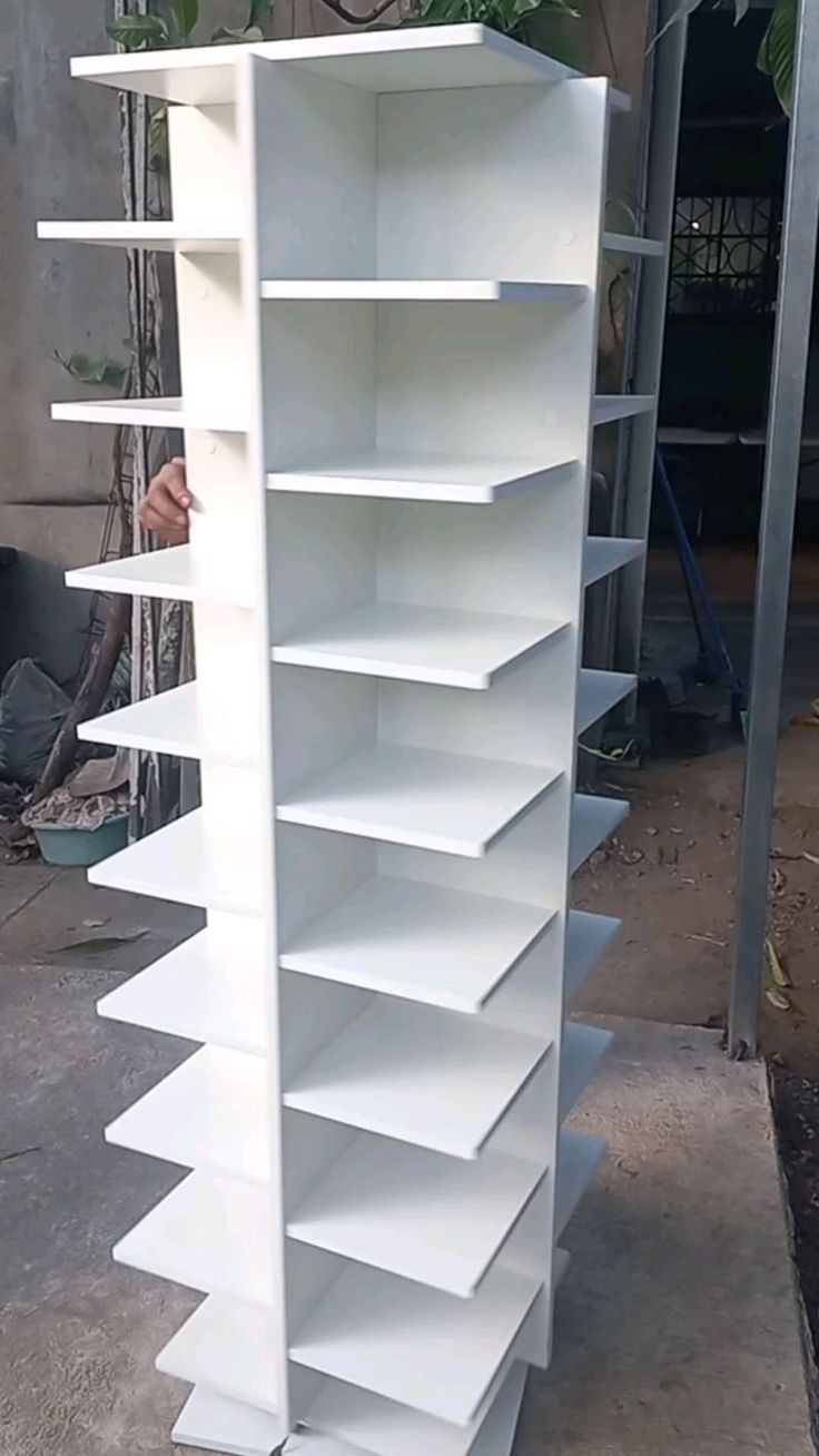 a white book shelf sitting on top of a cement floor next to a potted plant