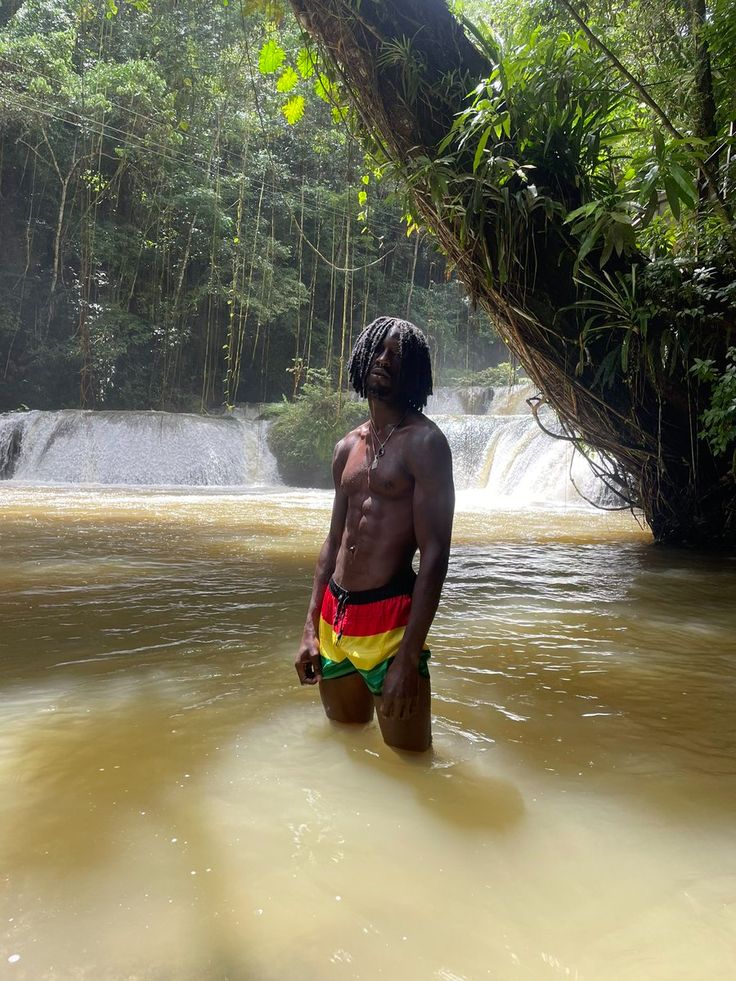 a man with dreadlocks standing in the middle of a river next to a waterfall