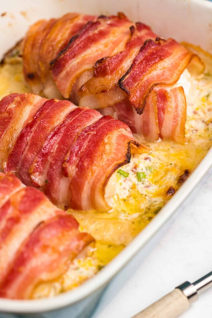 bacon wrapped chicken casserole in a white dish with utensils on the side