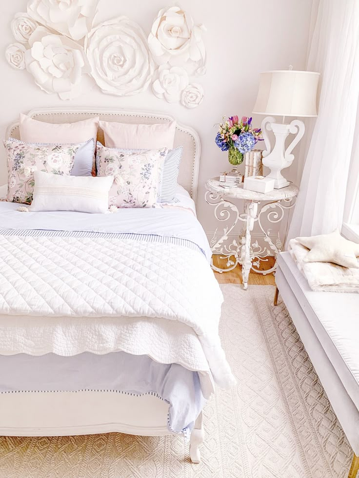 a white bed sitting in a bedroom next to a lamp and table with flowers on it