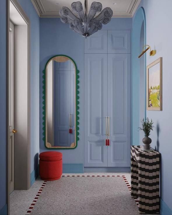 a hallway with blue walls and a large mirror on the wall next to a red stool