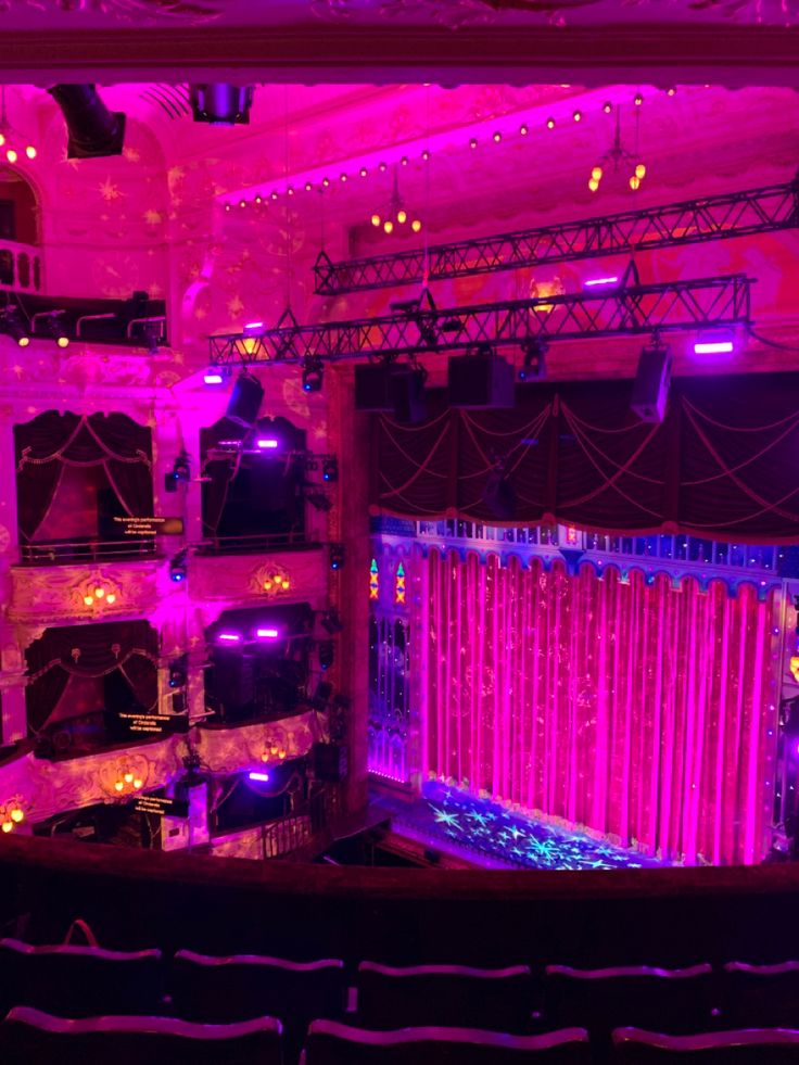 an auditorium filled with lots of purple lights and stage curtains on the side of it