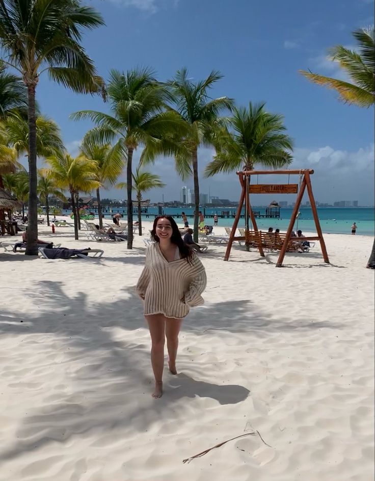 a woman standing on top of a sandy beach next to palm trees and the ocean