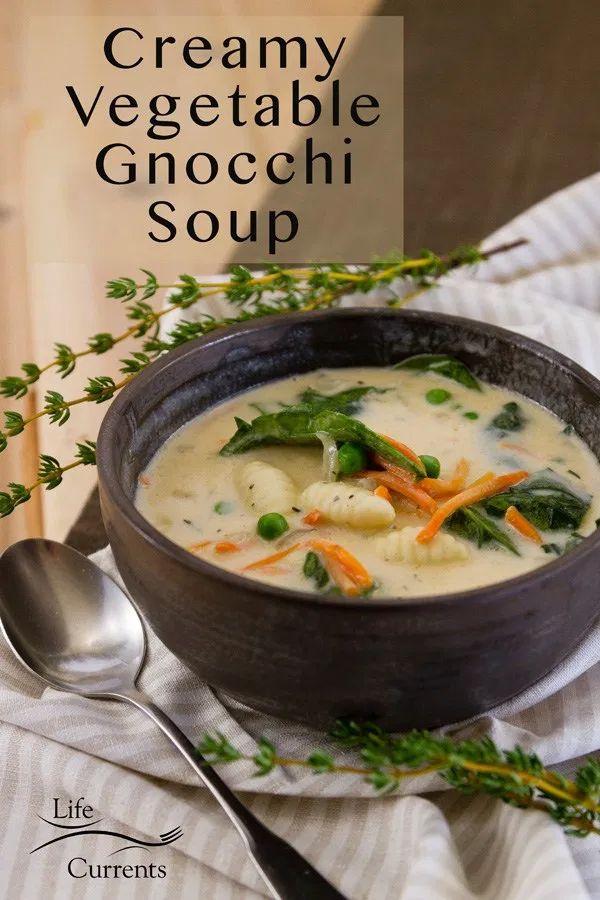 a bowl of creamy vegetable gnocchini soup on a table with a spoon