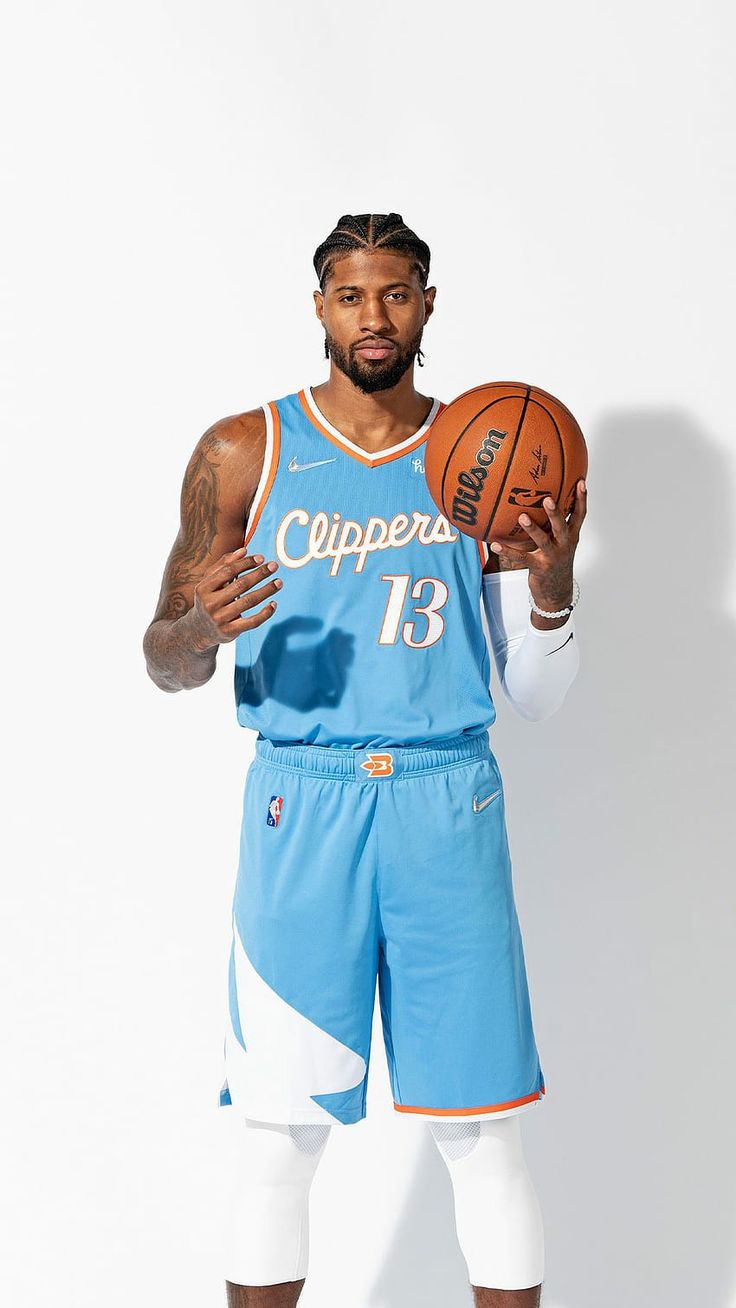 a man holding a basketball while standing in front of a white wall with his hands up