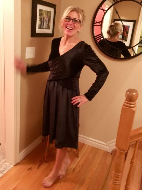 a woman standing in front of a mirror wearing a black dress and holding her hands on her hips