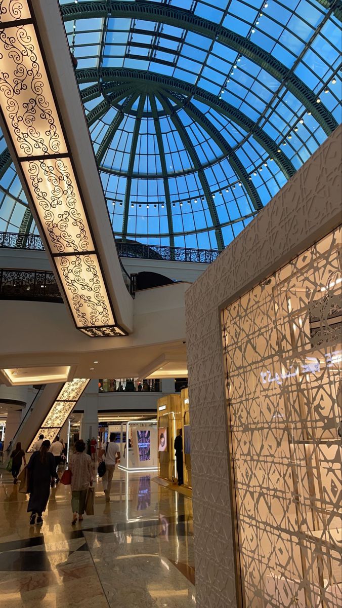 people are walking around in the lobby of a shopping mall with glass ceiling and skylights