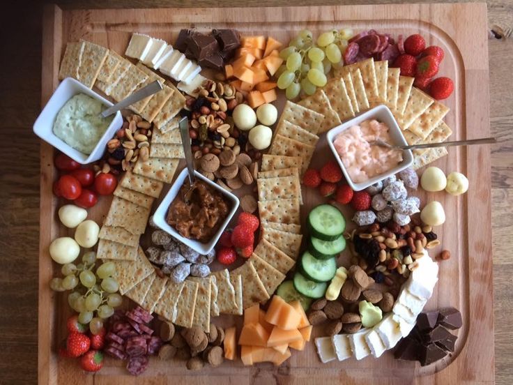 a platter with crackers, grapes, nuts, and dips on it