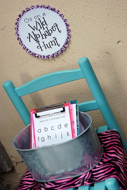 a metal bucket with magazines in it sitting on a chair next to a sign that reads wild alphabet hunt