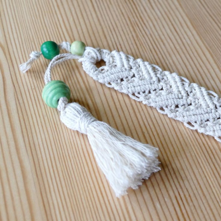 a white crochet tassel with green beads on it sitting on a wooden table