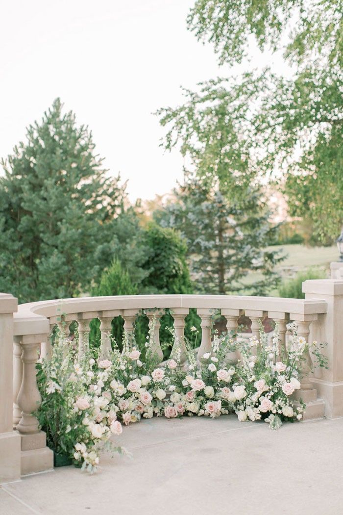 a bride and groom standing on a bridge with flowers in the foreground, surrounded by greenery