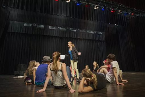 a group of young people sitting on the floor in front of a stage with lights