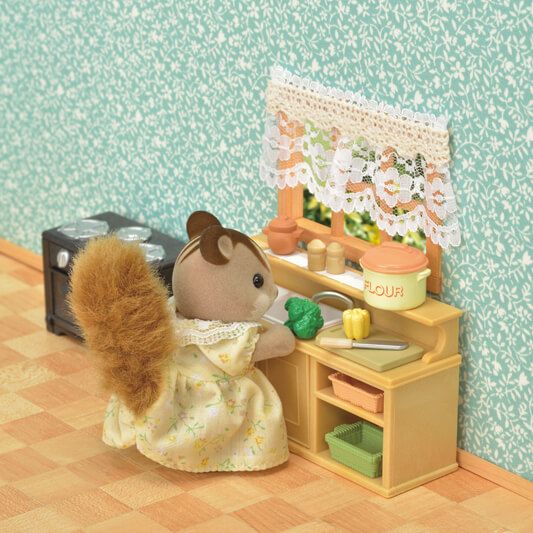 a toy mouse is sitting in front of a doll's kitchen