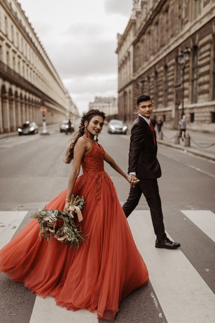 a man and woman in formal wear walking across a cross walk holding hands with each other