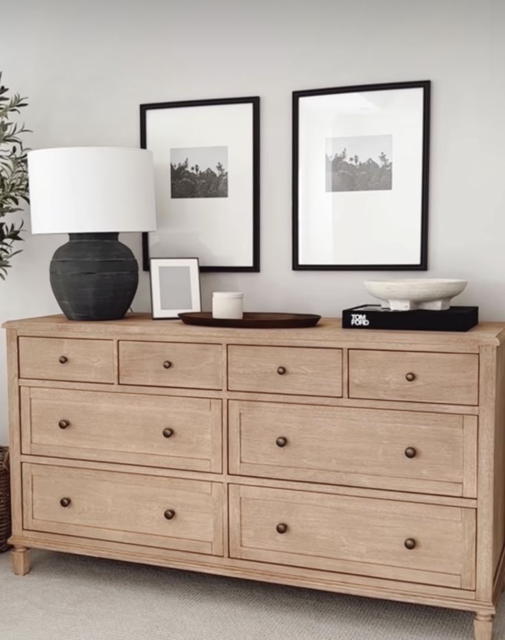 a large wooden dresser with two pictures on the wall above it and a lamp next to it