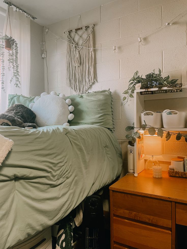 a bed with green sheets and pillows next to a wooden dresser in a white walled room